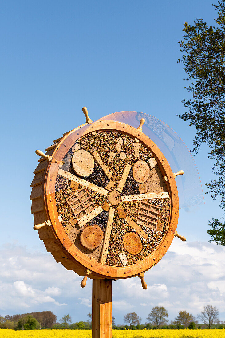 Insect hotel in the shape of a steering wheel at the edge of a rape field