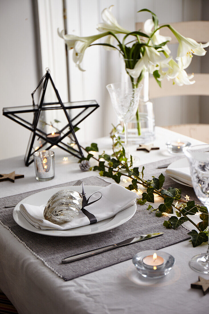 Gedeckter Tisch mit Teelichtern, Efeuranken, weißer Lilie und Stern