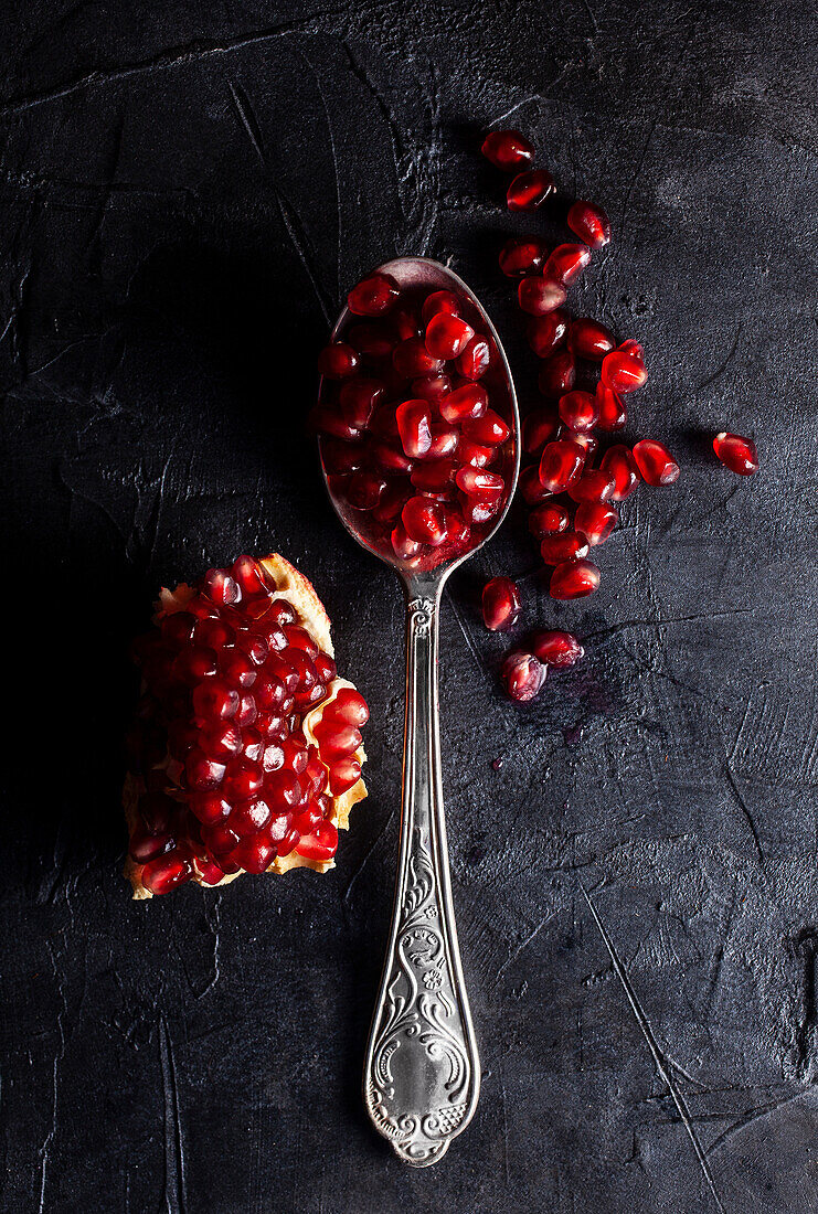 Open pomegranate and pomegranate seeds on a spoon