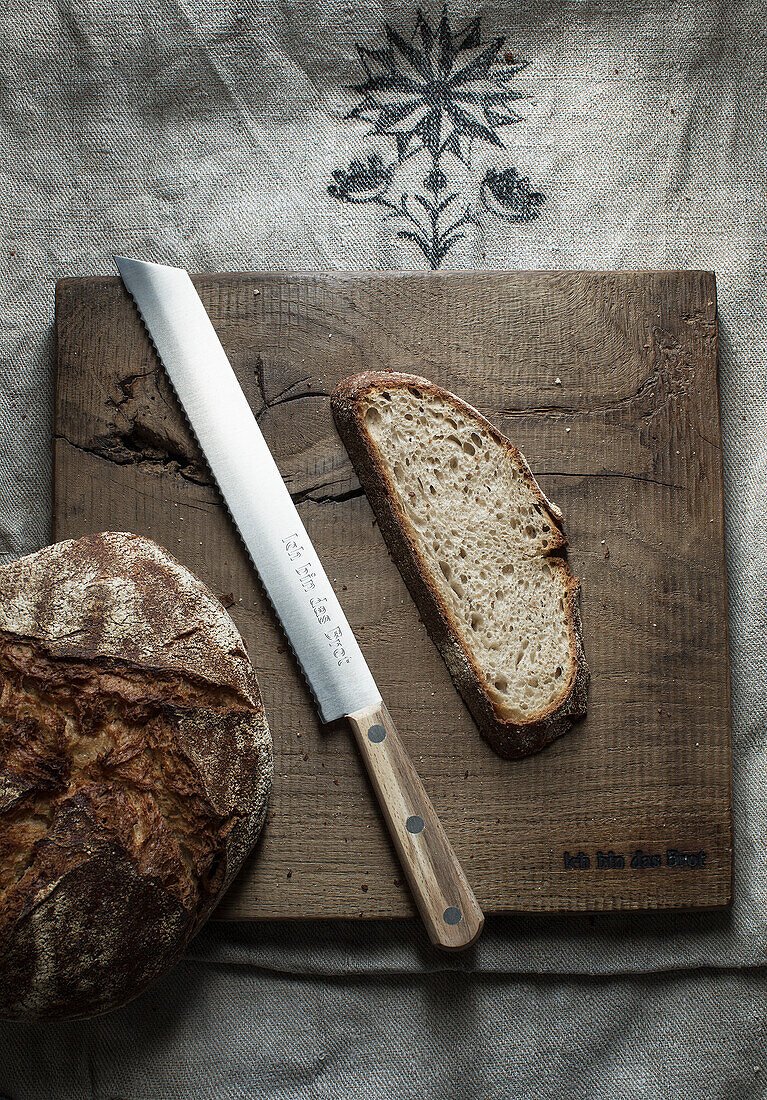 Rustic bread loaf and slice with knife on wooden board