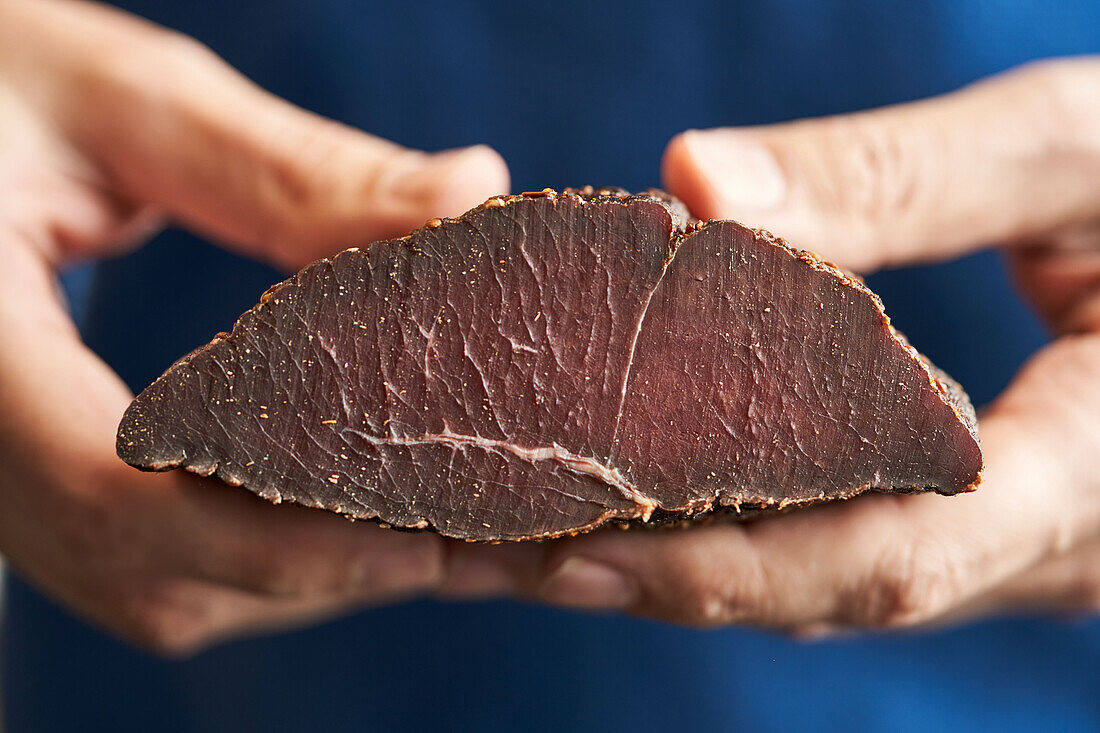 Hand holding a piece of cured venison ham