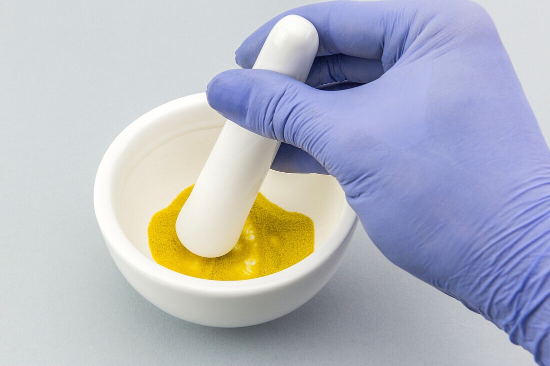 Scientist grinding yellow powder in a white mortar