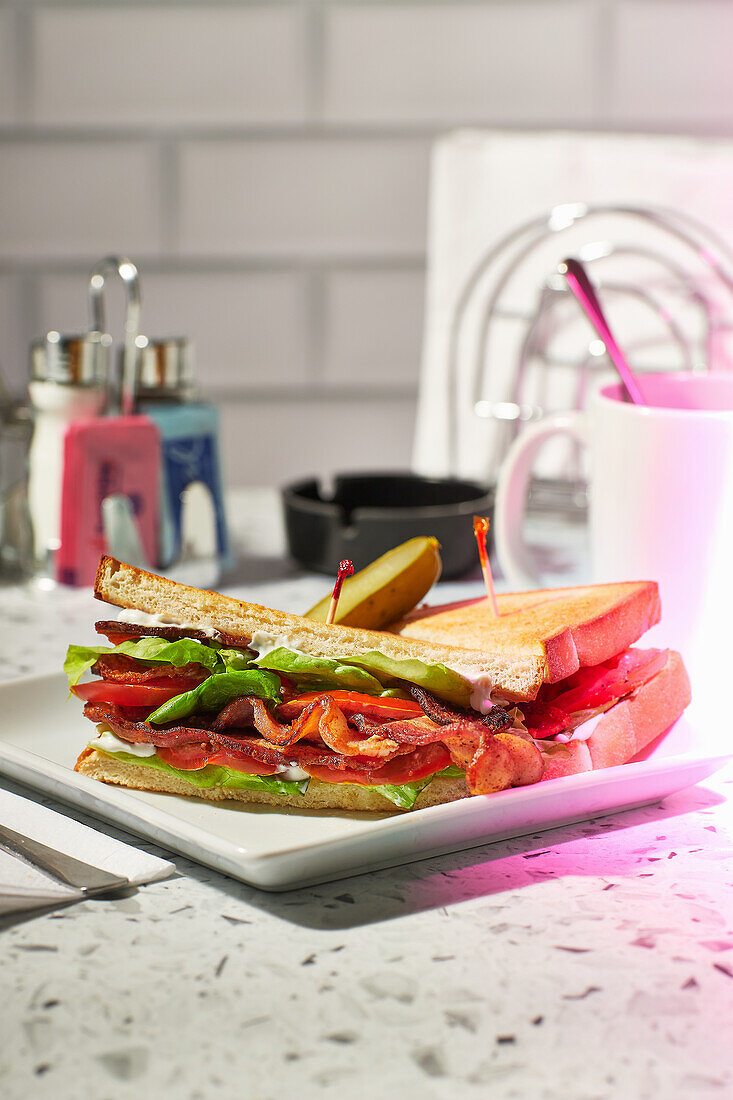 BLT-Sandwich mit Gurke auf Bistrotisch