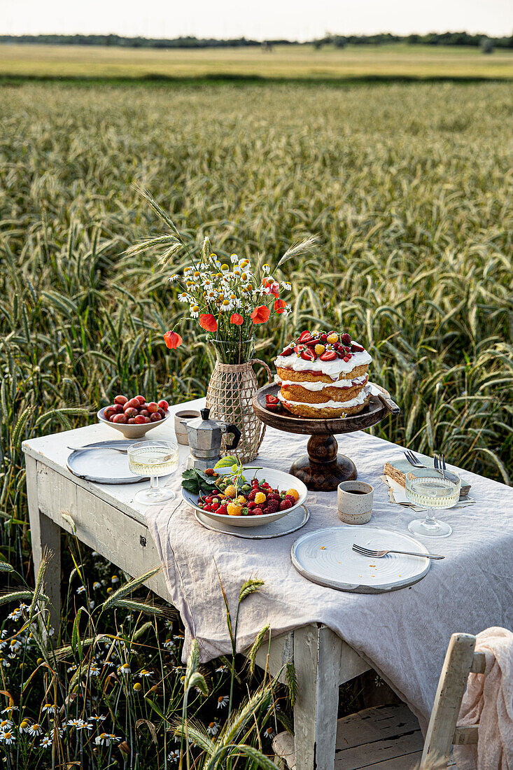 Set table with cake, bouquet and berries in the middle of a field