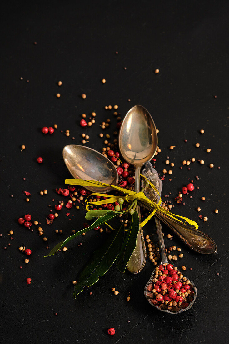 Coriander, mustard seeds and pink pepper on three silver spoons with bay leaves
