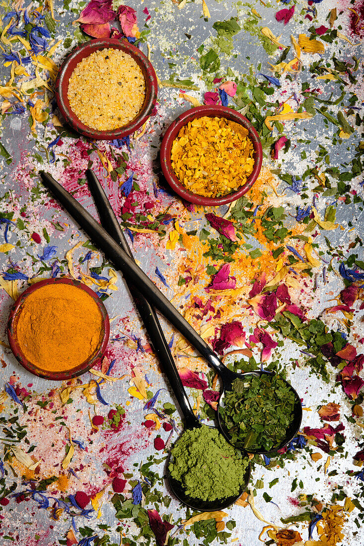 Teller mit Curry und zwei schwarze Löffel mit Stevia und Bärlauch auf getrockneten Blüten