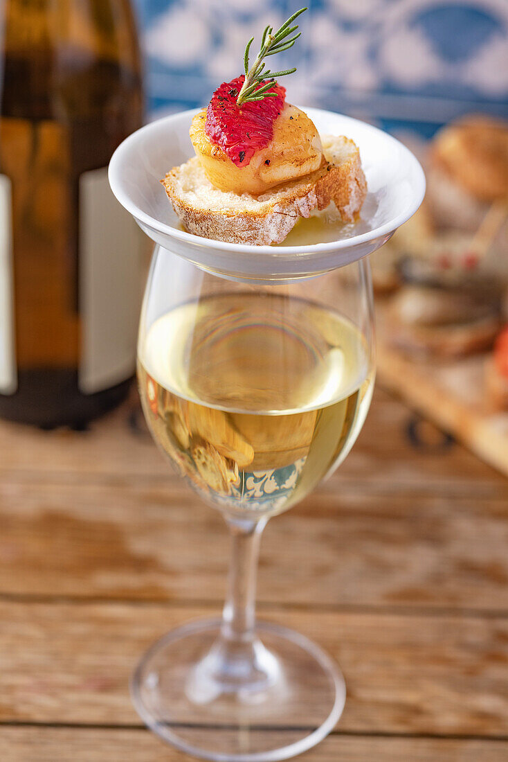 A glass of white wine and pincho made of crostini with scallop and blood orange