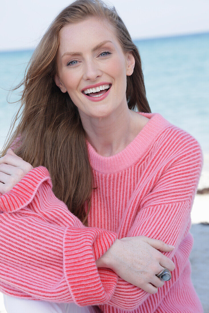 Good-humoured young blond woman in pink jumper by the sea