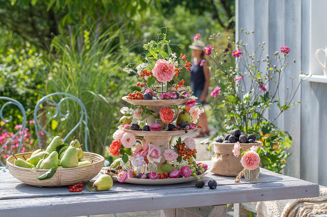 Etagere mit Rosenblüten, Strohblumen, Duftwicken, Hagebutten und Herbstfrüchten als Tischdekoration