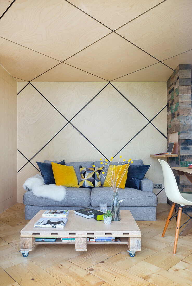 Grey upholstered sofa and pallet table in open-plan living room, diamond-shaped ceiling with LED strips