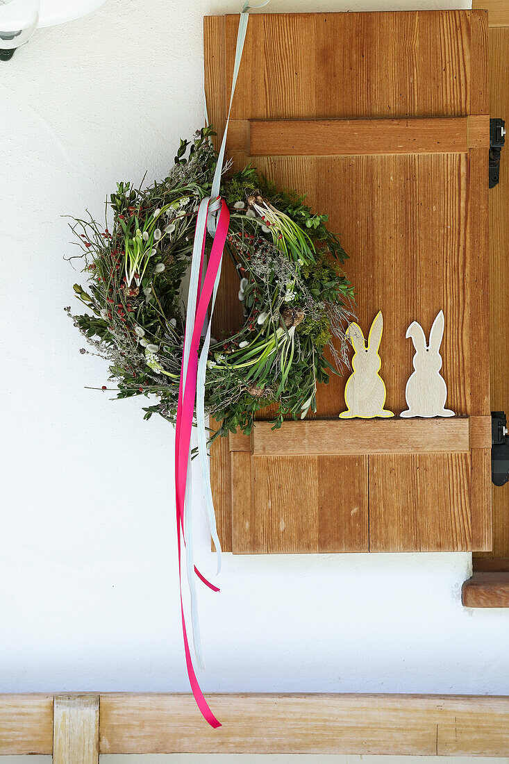 Österlich dekorierter Fensterladen mit Blumenkranz und Hasenfiguren