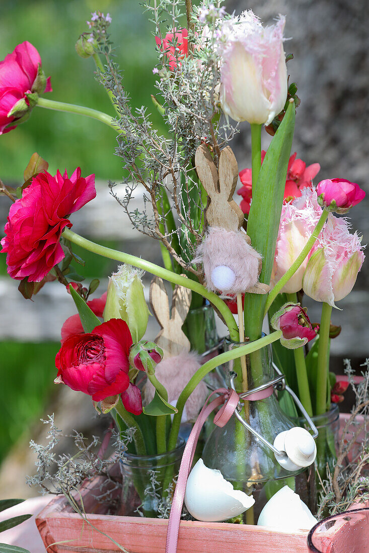 Glass bottle vases with spring flowers and Easter bunny in a planter