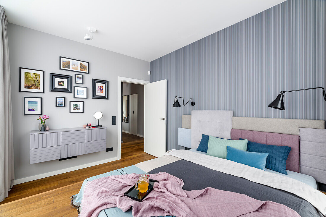 Queen bed with headboard made of several upholstered elements, mounted dresser, above photo gallery wall