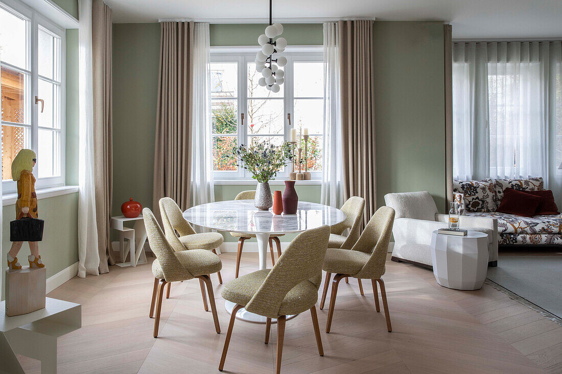 Classic table with marble top and upholstered chairs in the dining area with green walls