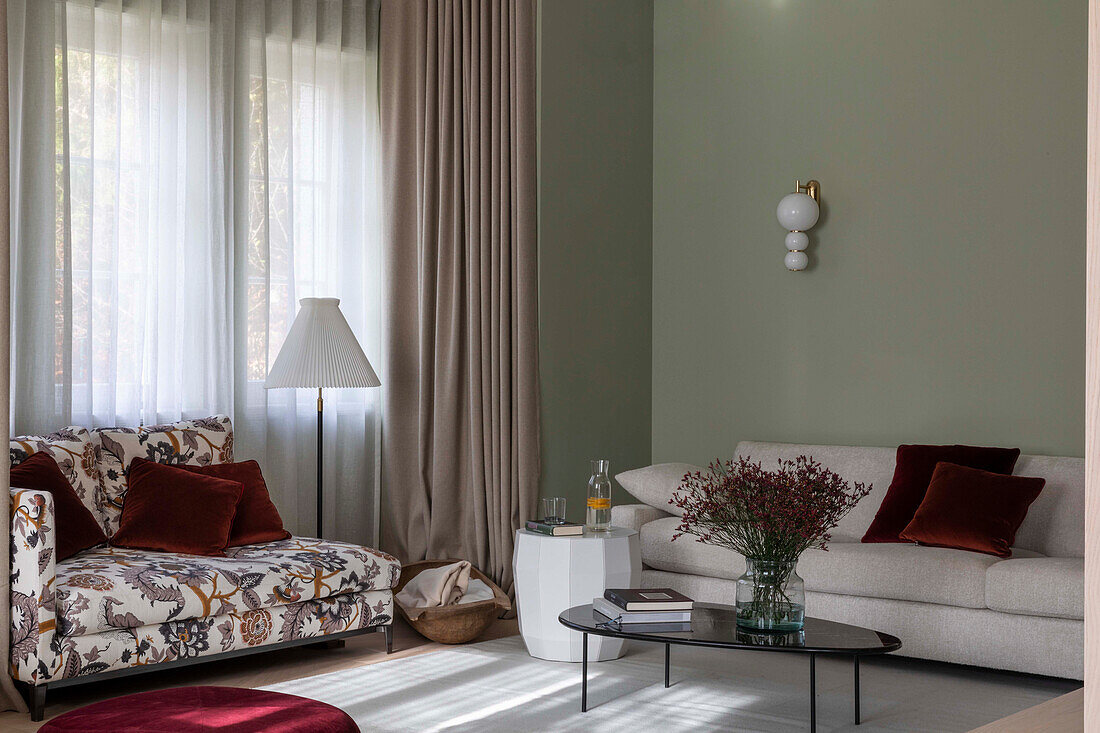 Floral sofa, light-colored sofa and coffee table in living area with floor-length curtains and green walls