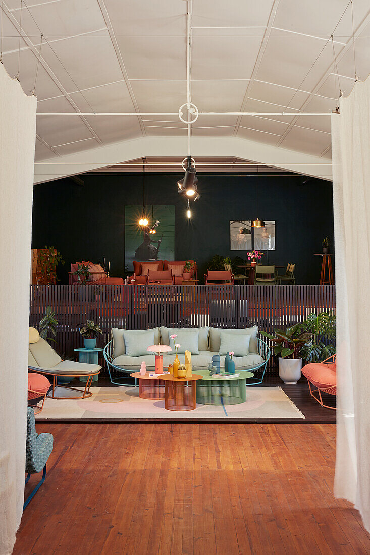 Wohnzimmer-Setup mit pastellfarbenen Möbeln im Vordergrund und dunklerer Raumgestaltung im Hintergrund