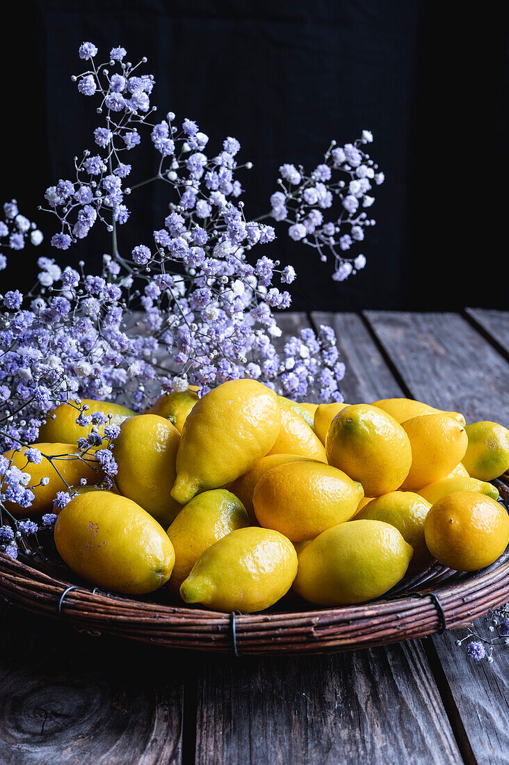 Frische Mini-Zitronen in Korbschale dahinter Blüten