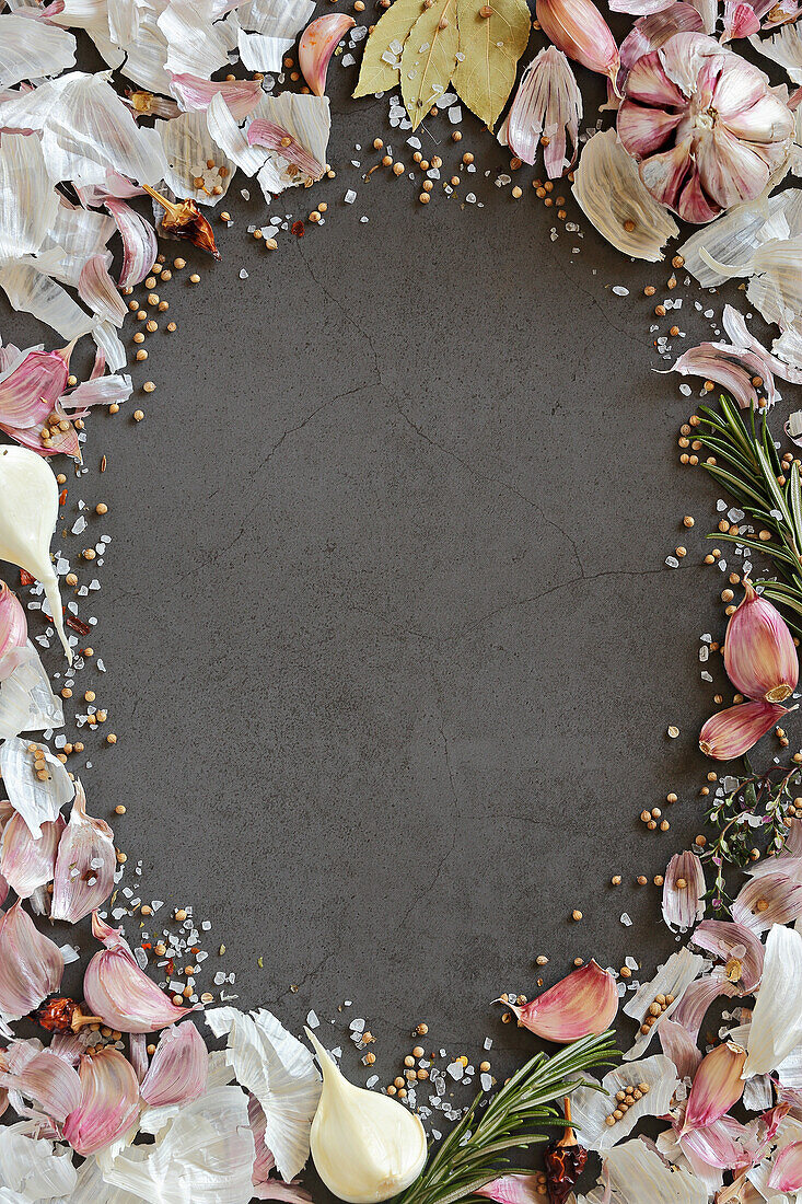 Garlic, garlic skins, herbs and spices creating an oval picture border