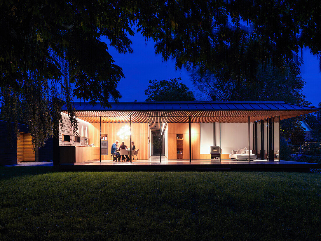 View at dusk from the garden into the living house with illuminated interiors