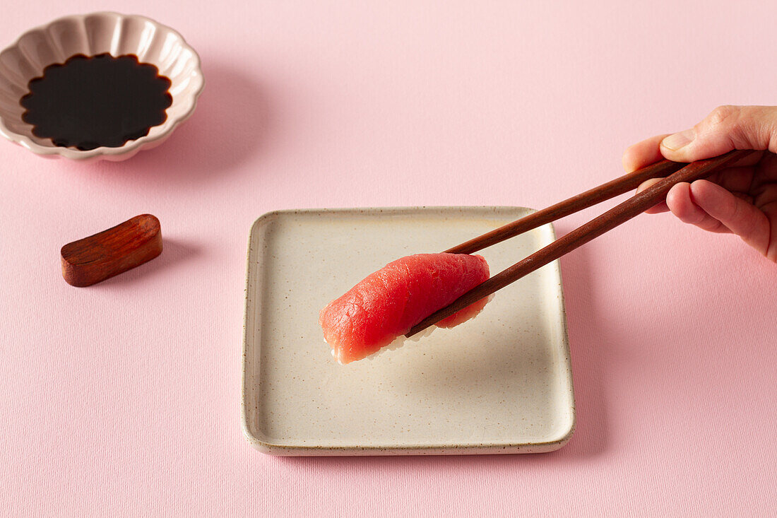 Hand hält Essstäbchen mit Nigiri-Sushi