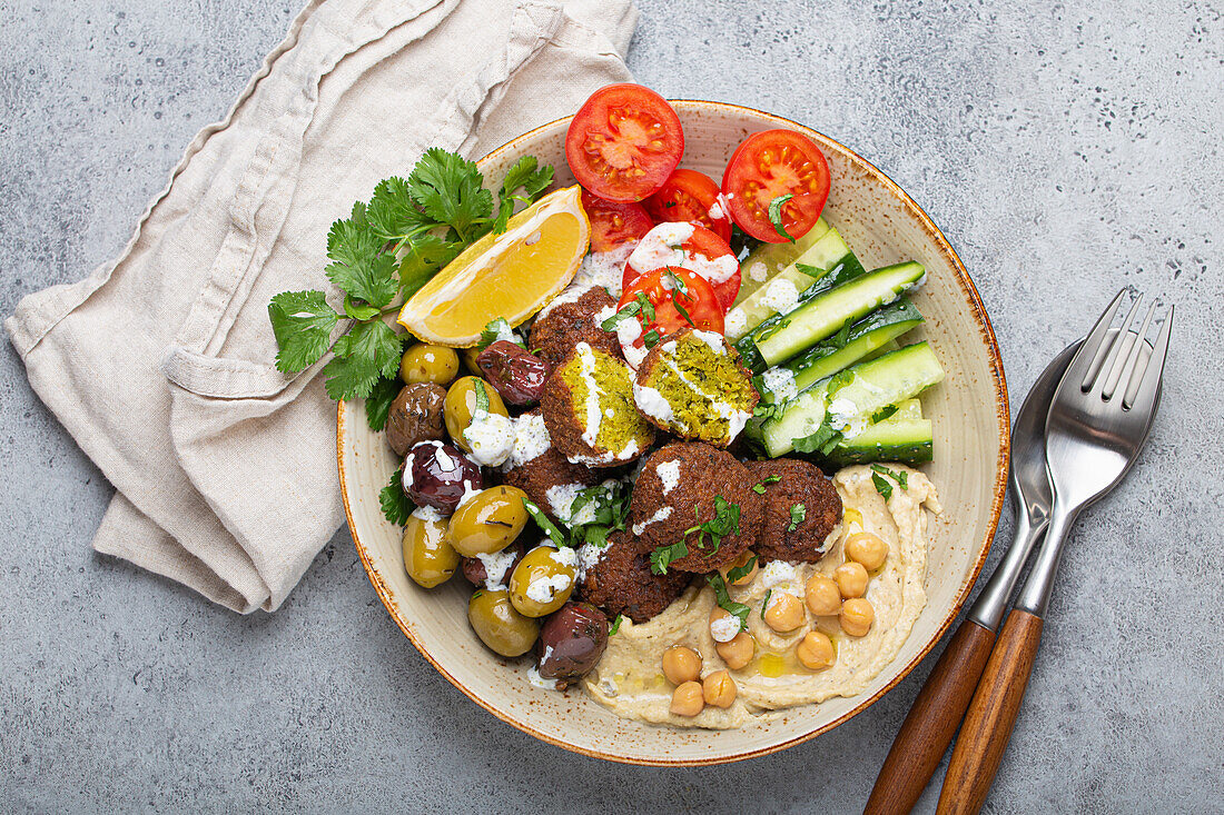 Falafel bowl with hummus, vegetables, olives, herbs and yogurt sauce