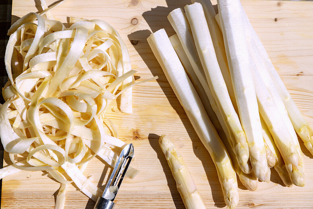 White asparagus, peeled, with peeler on wooden board outside