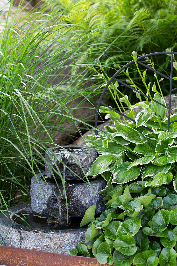 Stone water fountain surrounded by grasses and plants