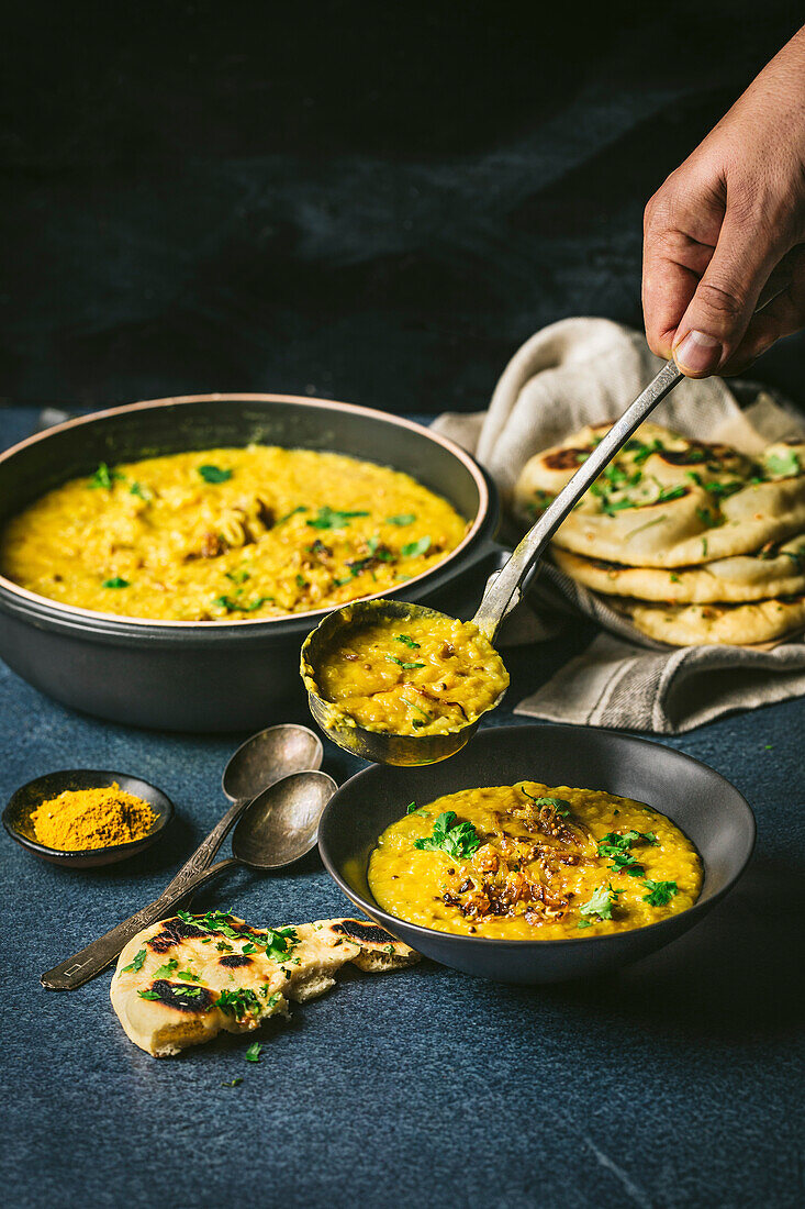 Curried yellow lentils in a large bowl spooned into a serving bowl with naan bread