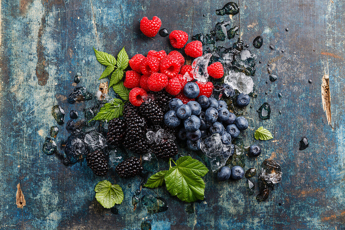 Fresh berries with leaves and ice on a blue wooden background