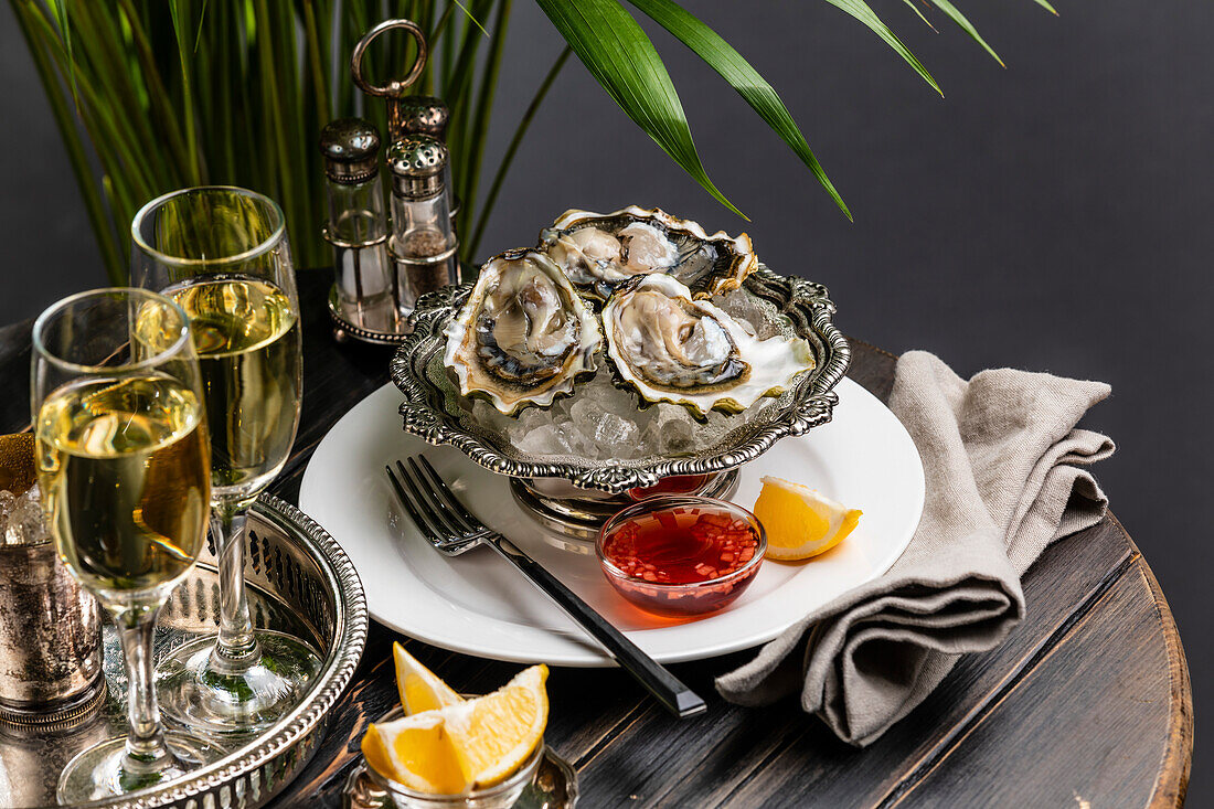 Fresh oysters on ice in a silver bowl next to champagne