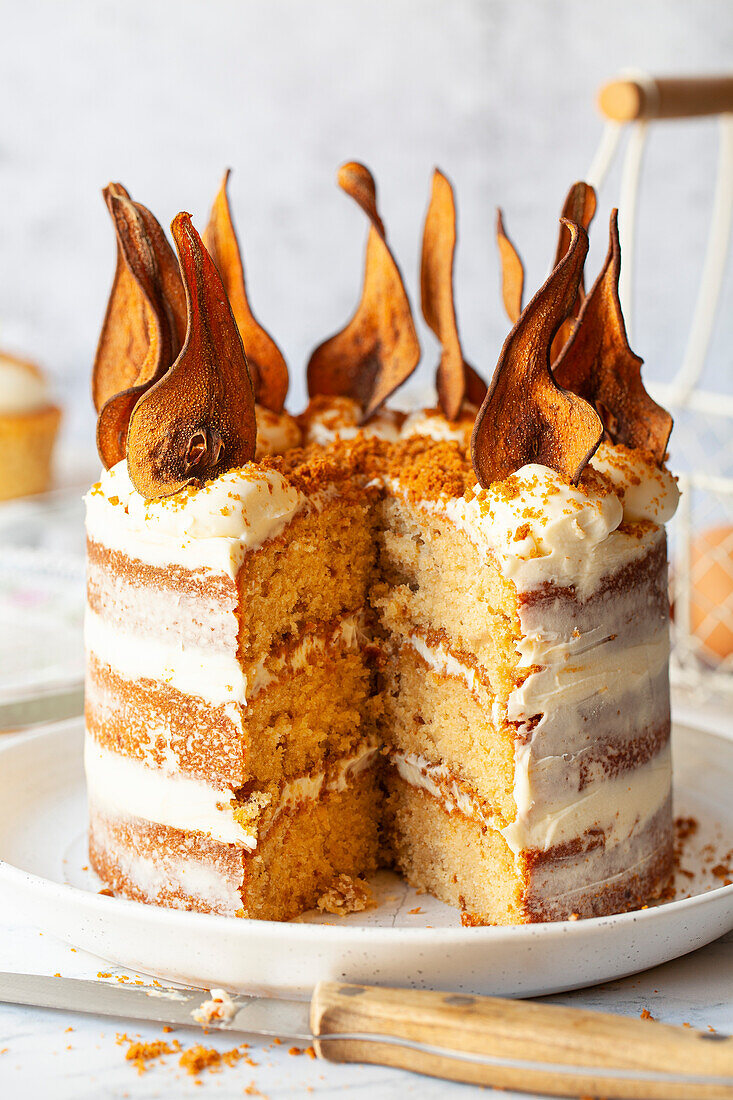 A layer cake decorated with buttercream frosting, cookie crumbs and oven dried pear wafers. A slice has been removed.