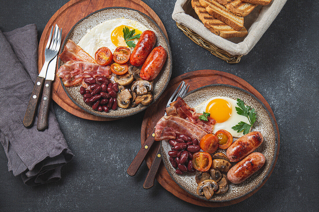 Englisches Frühstück mit Spiegeleiern, Würstchen, Bohnen, Pilzen, gegrillten Tomaten, Speck und Toast