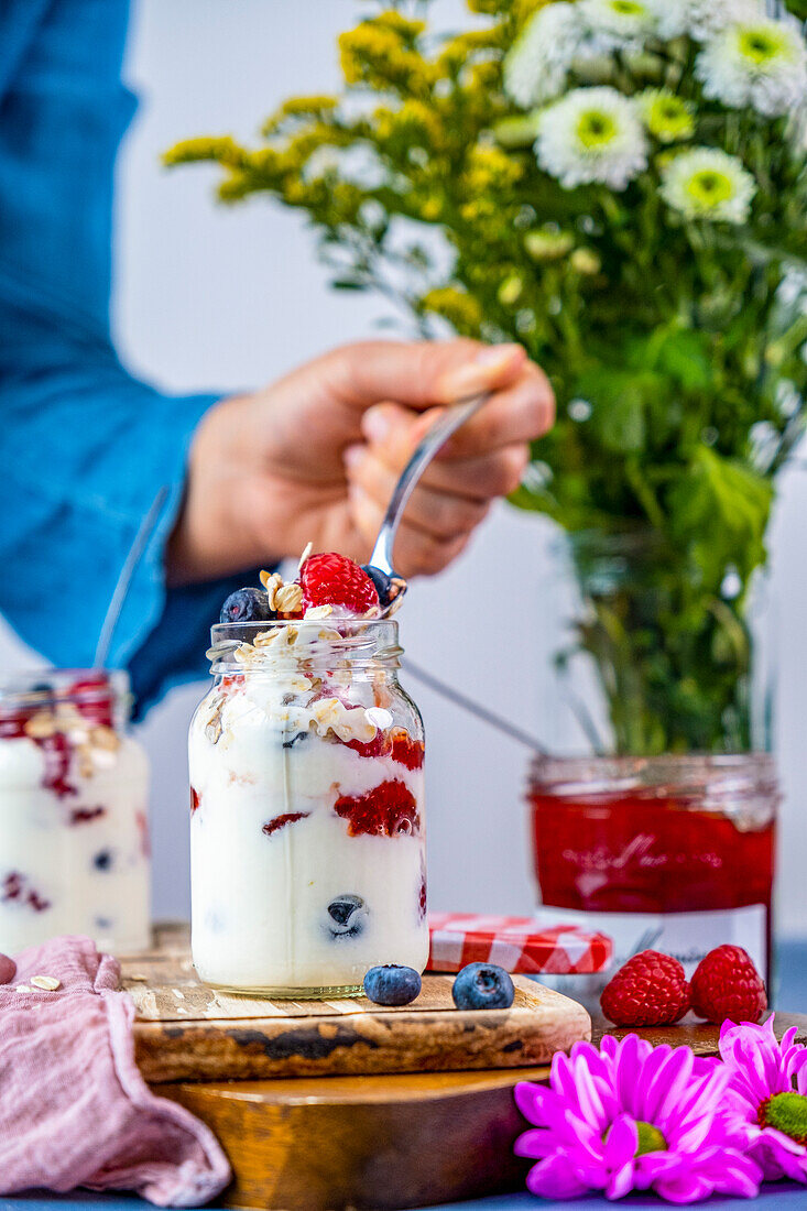 Joghurt im Glas mit Müsli, Erdbeermarmelade, Himbeeren und Heidelbeeren