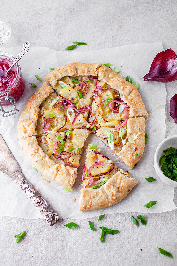 Kartoffelgalette mit eingelegten roten Zwiebeln und grünen Frühlingszwiebeln