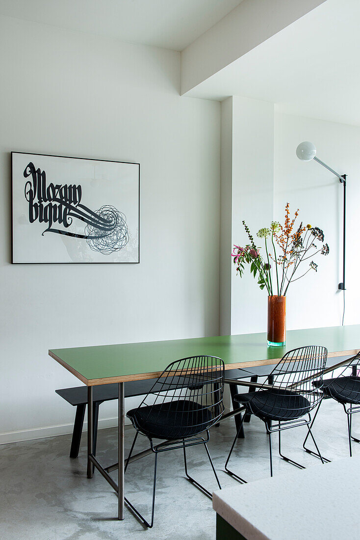 Dining table with green table top, black chairs, flowers and picture