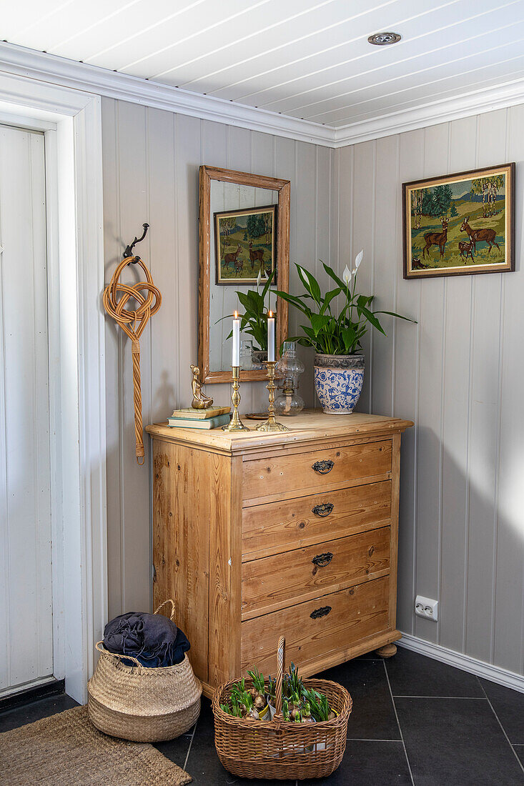 Wooden chest of drawers with mirror and decorative objects in light-coloured hallway