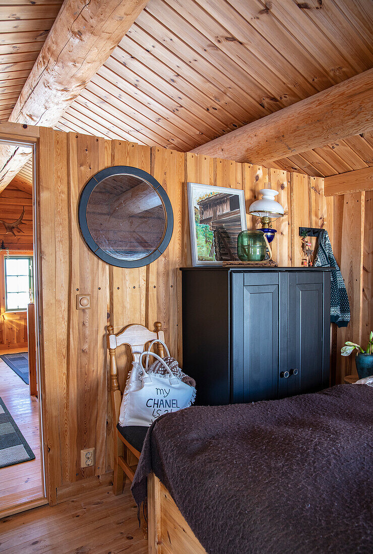 Holzvertäfeltes Schlafzimmer mit rundem Spiegel und schwarzer Kommode
