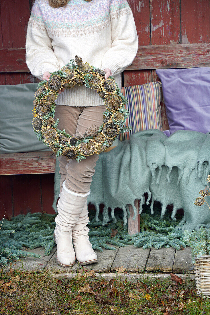 Person holding a homemade wreath in front of a rustic wooden wall