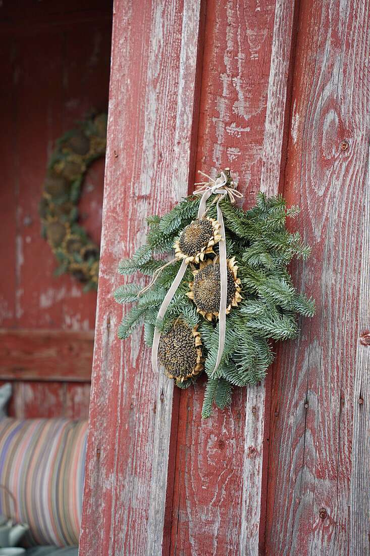 Türkranz aus Tannenzweigen und getrockneten Sonnenblumen an roter Holzwand