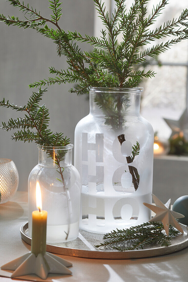 Vases with fir branches on a round tray, candle lit in front of them