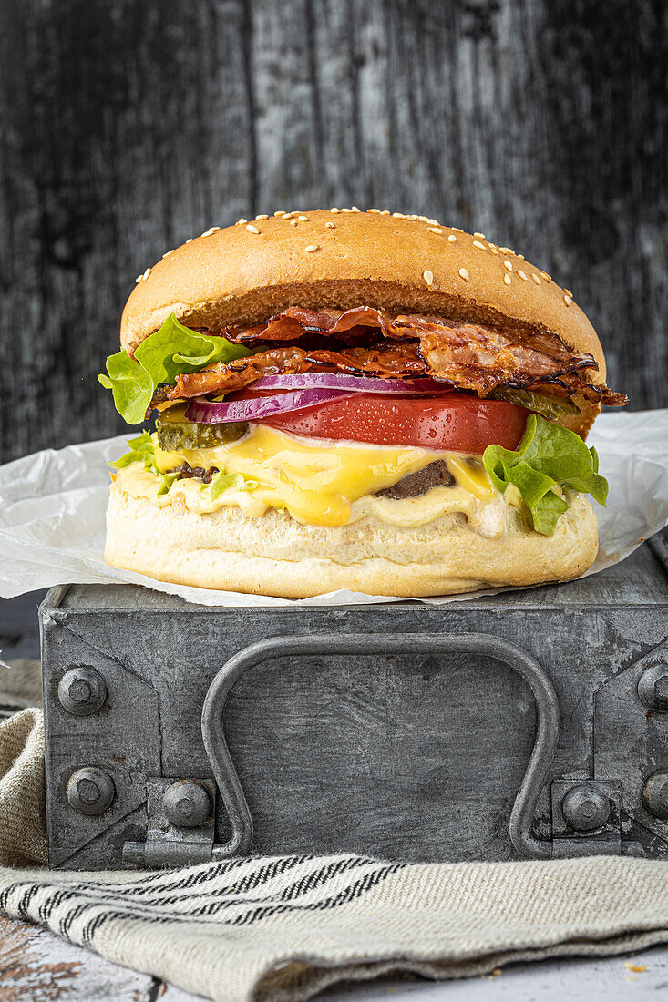 Cheeseburger mit Rind, Speck, Tomaten, roten Zwiebeln und Gewürzgurken