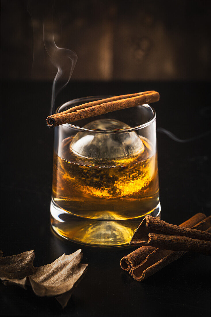 Glass of whiskey with ice ball and lit cinnamon stick