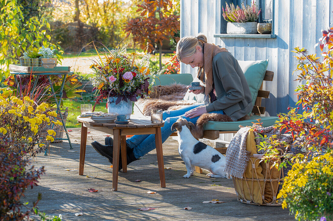 Woman on autumnal terrace with dog and flower decoration