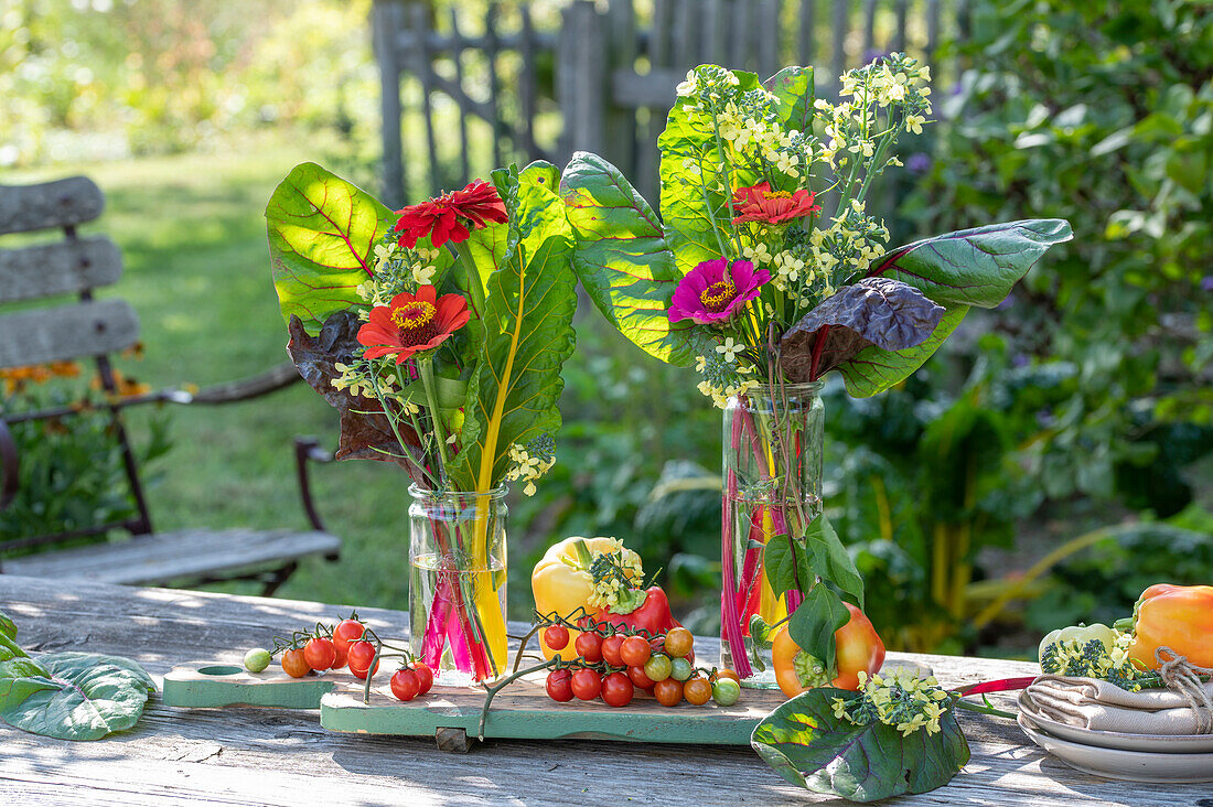 Otudoor dining table decoration with bouquet of pinnacles (Zinnia) and chard leaves, cutting board with tomatoes, peppers
