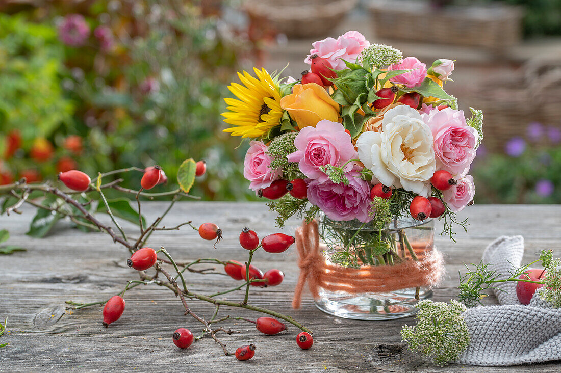 Blumenstrauß aus Rosen (Rosa), Hagebutten, Sonnenblumen (Helianthus), Wilde Möhre auf Gartentisch