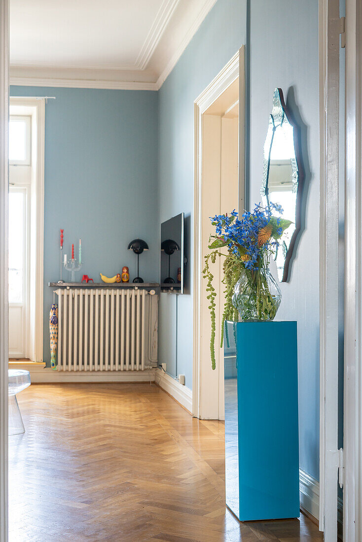 Blue plinth with bouquet of flowers, wooden floor and light blue walls