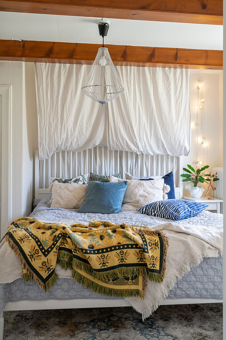 Bed with patterned bedspread and pendant light in bedroom with ceiling beams