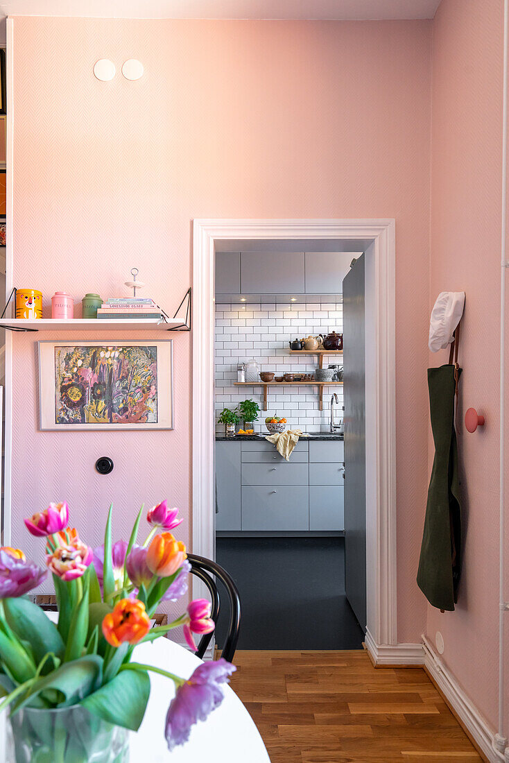 Room in pastel pink with a view of the kitchen and a bouquet of tulips on the table