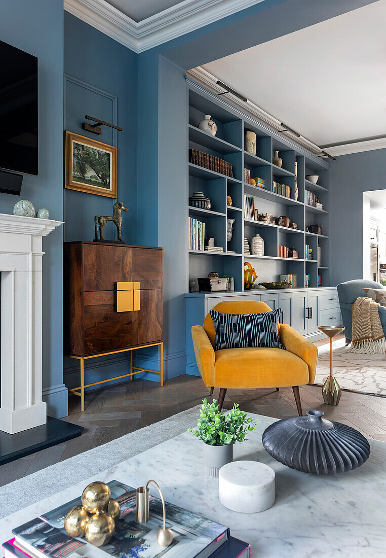 Blaue Regalwand, elegantes Highboard und gelber Sessel im Wohnzimmer