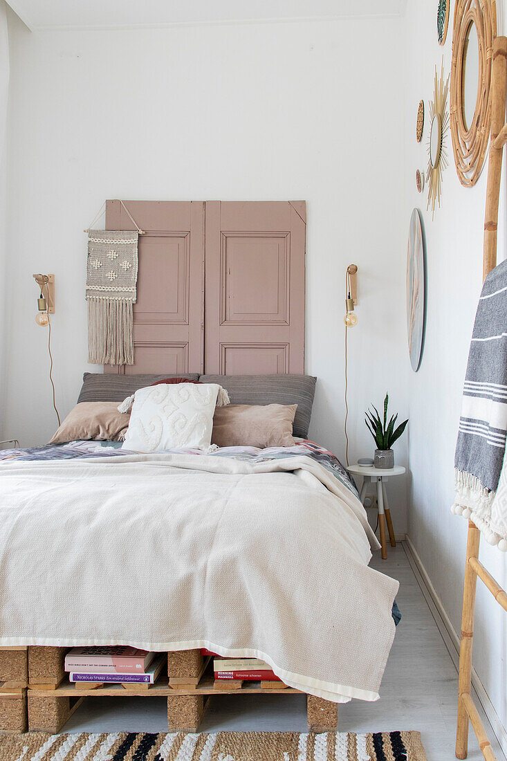 Helles Schlafzimmer mit Palettenbett und rosa Fensterläden als Deko